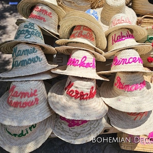 Könnte beinhalten: Eine Sammlung von Strohhüten mit bunten Stickereien. Die Hüte sind übereinander gestapelt, wobei der oberste Hut den Text "Habibi" zeigt.