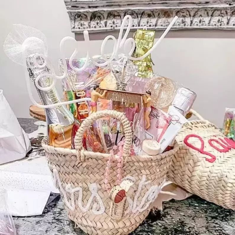 K&ouml;nnte beinhalten: Ein Weidenkorb gef&uuml;llt mit Geschenken f&uuml;r eine Brautparty. Der Korb ist mit den Worten "Mrs. to Be" verziert und enth&auml;lt eine Flasche Champagner, ein Glas und andere Partygeschenke.