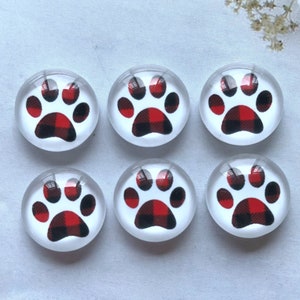 Op de afbeelding: Zes ronde glazen cabochons met een witte achtergrond en een rood en zwart buffalo plaid-pootafdruk ontwerp.
