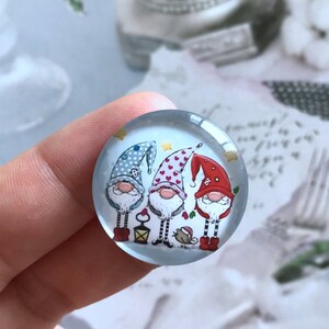 May include: Three gnomes with red, blue, and white hats stand together. The gnome on the left is wearing a blue hat with white polka dots, the middle gnome is wearing a red hat with white hearts, and the gnome on the right is wearing a red hat with white stars. The gnomes are holding a lantern and a bird.