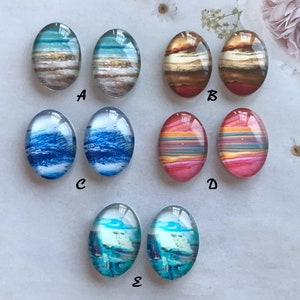 May include: Set of 10 oval-shaped glass cabochons with various abstract designs. The cabochons feature a variety of colours, including blue, brown, red, pink, and white. The cabochons are arranged in pairs, labelled A through E.