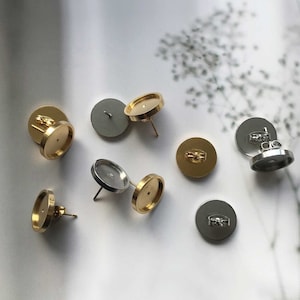 Puede incluir: Un conjunto de ocho engastes para pendientes de oro y plata. Los engastes son redondos y tienen una parte posterior plana. Están diseñados para sujetar una variedad de cabujones.