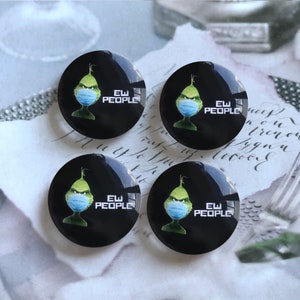 May include: Four circular black buttons featuring a green character wearing a blue face mask. Each button displays the text "EW PEOPLE" in white capital letters next to the character. The buttons have a glossy finish and a smooth, rounded surface.