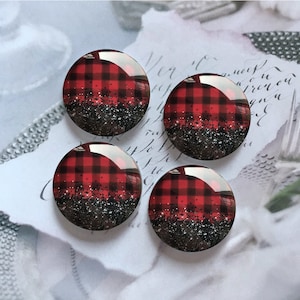 Puede incluir: Cuatro cabujones redondos de resina, a cuadros rojos y negros, con purpurina negra. Los cabujones miden aproximadamente 2,5 cm de diámetro.