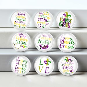 May include: Nine circular glass magnets with Mardi Gras designs. Each magnet has text and graphics in purple, green, and gold. Phrases include "Mardi Gras," "Laissez les bon temps rouler," and "May contain alcohol."