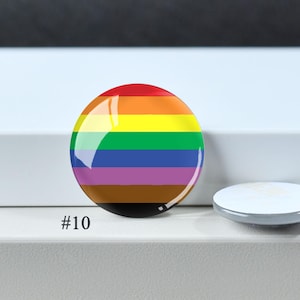 Puede incluir: Un bot&oacute;n circular con un patr&oacute;n de rayas horizontales en rojo, naranja, amarillo, verde, azul, morado, marr&oacute;n y negro. El bot&oacute;n tiene un acabado brillante y est&aacute; etiquetado con el n&uacute;mero #10 en la esquina inferior izquierda.