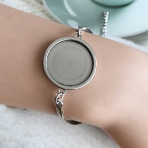 Può includere: Un braccialetto argentato con una grande lunetta rotonda e vuota. Il braccialetto ha un design semplice con una catena e una barra curva. La lunetta è pronta per un inserto personalizzato, ideale per gioielli personalizzati.