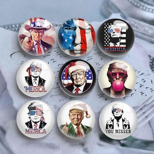 May include: Set of 9 round, glass button pins featuring various images of a man with a red, white, and blue American flag theme. The images include the man wearing sunglasses, a Santa hat, and a cowboy hat. Some of the pins have the word "MERICA" on them. One pin has the text "YOU MISSED".