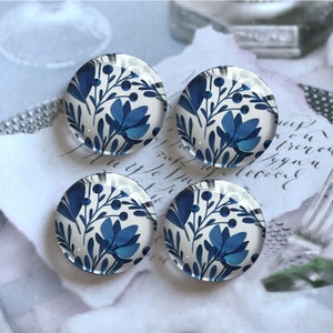 Könnte beinhalten: Vier runde Glascabochons mit weißem Hintergrund und einem blauen Blumenmuster. Die Cabochons haben einen Durchmesser von etwa 2,5 cm.