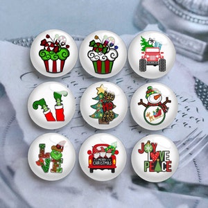 Puede incluir: Nueve cabujones redondos de vidrio con temática navideña con varios diseños. Los diseños incluyen un Jeep rojo con un árbol de Navidad, un muñeco de nieve, cupcakes y el texto "JOY LOVE PEACE". Otros diseños incluyen un árbol de Navidad y piernas de elfo.