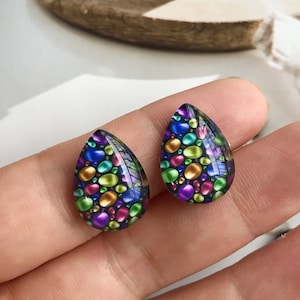 May include: A pair of teardrop-shaped earrings with a colorful mosaic pattern of small, round, iridescent stones on a black background.