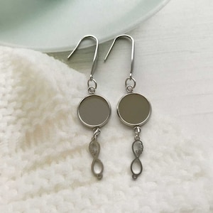 May include: A pair of silver earrings with round, clear glass charms and infinity symbol charms hanging from them.