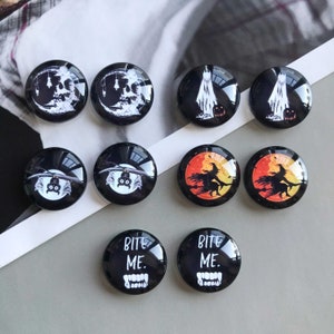May include: Eight round, black and white Halloween themed glass cabochons with various images including a skull, a ghost, a bat, a witch, and the text "Bite Me".