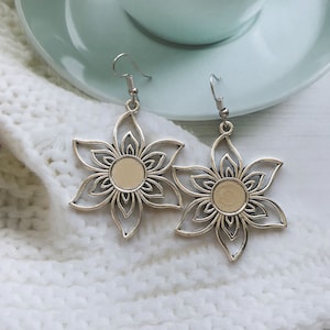 May include: A pair of silver earrings with a delicate flower design. Each earring features a circular center with a cutout pattern.