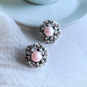 Pode incluir: Um par de brincos de prata com detalhes de flores cor-de-rosa e uma pérola no centro de cada brinco.