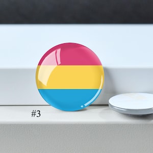 Puede incluir: Un bot&oacute;n circular con un dise&ntilde;o tricolor horizontal que presenta una franja superior magenta, una franja central amarilla y una franja inferior cian. El bot&oacute;n tiene un acabado brillante y est&aacute; marcado con el n&uacute;mero 3 en la esquina inferior.