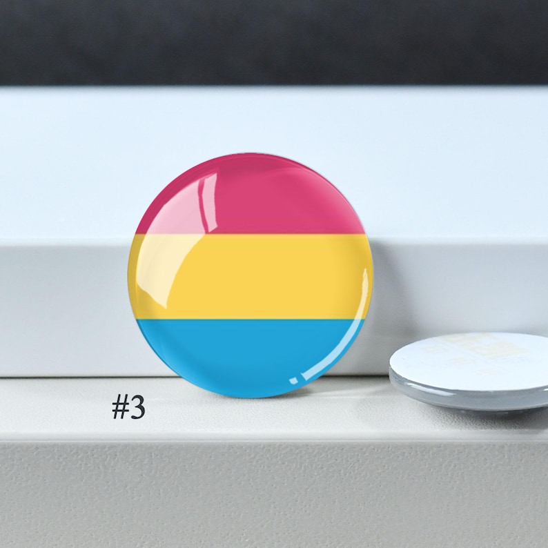 Puede incluir: Un bot&oacute;n circular con un dise&ntilde;o tricolor horizontal que presenta una franja superior magenta, una franja central amarilla y una franja inferior cian. El bot&oacute;n tiene un acabado brillante y est&aacute; marcado con el n&uacute;mero 3 en la esquina inferior.
