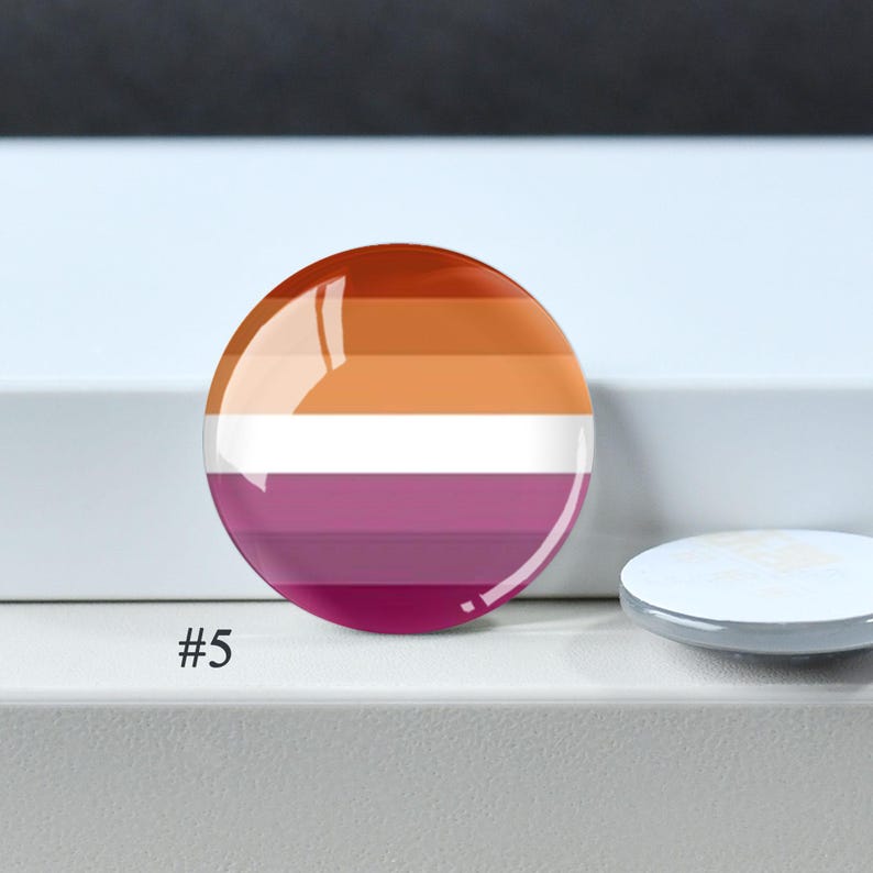 Puede incluir: Una chapa redonda con un patr&oacute;n de rayas horizontales en tonos naranja oscuro, naranja claro, blanco, rosa claro y rosa oscuro. El n&uacute;mero #5 est&aacute; impreso en negro en la parte inferior izquierda de la chapa, que tiene un acabado brillante.