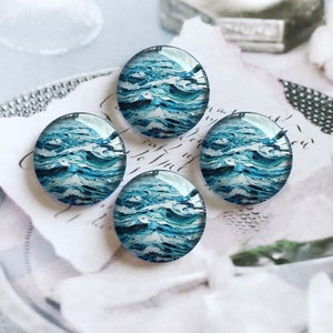 May include: A set of four circular glass cabochons featuring a vibrant abstract pattern of swirling ocean waves in shades of deep navy, bright turquoise, and crisp white, creating a textured appearance of moving water under a smooth dome.