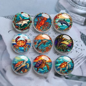 May include: Set of ten round glass cabochons with colorful stained glass designs of sea creatures. The designs include a shark, a lobster, a dolphin, a turtle, and a crab.