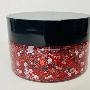 May include: A clear jar filled with red and white glitter. The jar has a black lid and is sitting on a white surface. The glitter appears to be a mix of shapes and sizes.