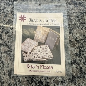 May include: A sewing pattern for a fabric-covered notebook, called "Just a Jotter", by Bits 'n Pieces. The pattern shows three notebooks in different fabric designs, including a floral pattern, a pattern with scissors and stamps, and a pattern with a map. The pattern is labeled with the title "Just a Jotter", the company name "Bits 'n Pieces", and the pattern number "#640".