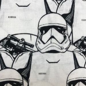 May include: Close-up of a white fabric with a repeating black and white illustration of Star Wars Stormtrooper helmets and blasters. The design features detailed line art of the iconic helmets.