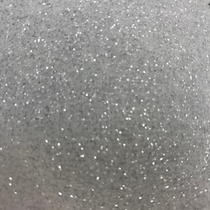 Könnte beinhalten: Nahaufnahme eines weißen Stoffes mit glitzernder, gesprenkelter Textur. Die Oberfläche ist mit winzigen, reflektierenden Partikeln bedeckt, die das Licht einfangen und einen schimmernden Effekt erzeugen. Das Gesamtbild ist weich und zart.