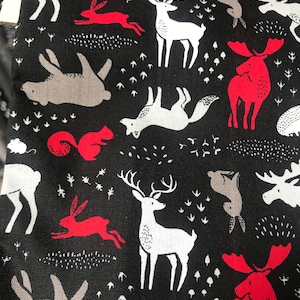 May include: Black fabric with a repeating pattern of woodland animals. White deer, gray rabbits, red squirrels and moose are scattered across the fabric. The design includes small white leaf and grass accents.