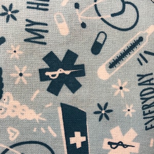 May include: Light blue fabric with a repeating pattern of medical symbols, including stethoscopes, pills, and thermometers. The words "MY HERO" and "EVERYDAY" are also printed on the fabric. White and teal colors.