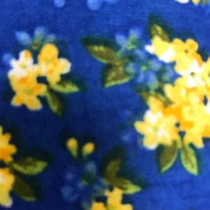 May include: A close-up of a fabric with a floral pattern. The design features clusters of yellow and blue flowers with green leaves against a deep blue background. The fabric has a soft, textured appearance.