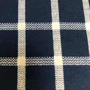 May include: Close-up of a navy blue and white checkered fabric. The fabric has a woven texture with a grid pattern. The white lines have a zig-zag design, creating a textured effect. The overall look is clean and classic.