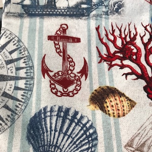 May include: A nautical-themed fabric featuring a repeating pattern of sailboats, anchors, compasses, seashells, and coral. The design incorporates shades of blue, red, and brown against a white and light blue striped background.