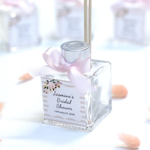 Peut inclure: Une petite bouteille en verre avec un couvercle argenté et un ruban rose. La bouteille porte une étiquette qui dit "Jasmine's Bridal Shower February 23, 2020".