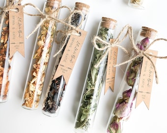 May include: Ten glass test tubes filled with different types of dried tea leaves and flowers. Each tube has a brown paper tag tied around it with the text "Let Love Brew" and the names "Bryan & Katie" and the type of tea.