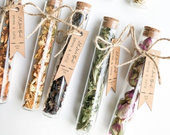 May include: Ten glass test tubes filled with different types of dried tea leaves and flowers. Each tube has a brown paper tag tied around it with the text "Let Love Brew" and the names "Bryan & Katie" along with the type of tea.