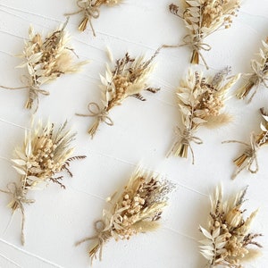 May include: A collection of ten small bouquets of dried flowers, each tied with twine. The bouquets are made up of various shades of beige, brown, and white dried flowers and grasses.