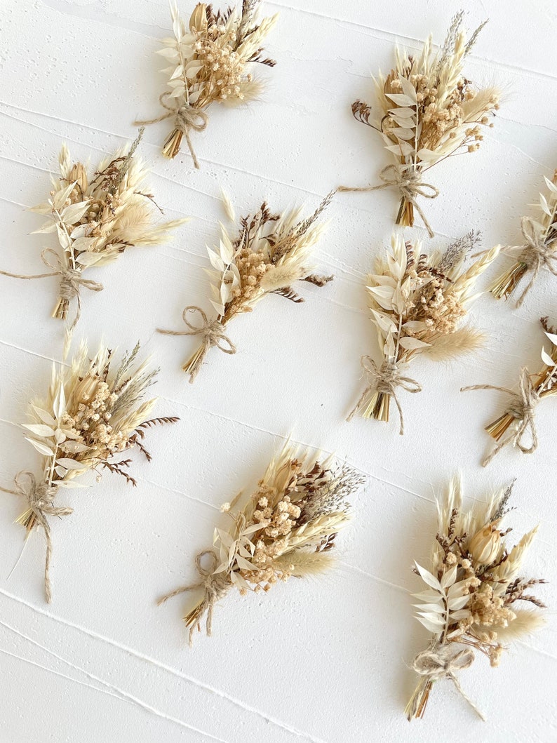 May include: A collection of ten small bouquets of dried flowers, each tied with twine. The bouquets are made up of various shades of beige, brown, and white dried flowers and grasses.