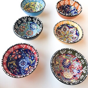 May include: Six small, round ceramic bowls with colorful floral patterns. The bowls have a variety of colors, including blue, red, orange, and green, with black or white rims. The bowls are likely for serving dips or small portions.