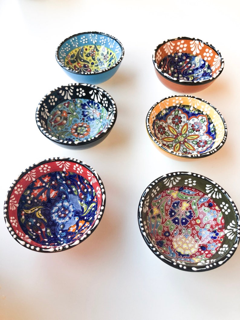 May include: Six small, round ceramic bowls with colorful floral patterns. The bowls have a variety of colors, including blue, red, orange, and green, with black or white rims. The bowls are likely for serving dips or small portions.