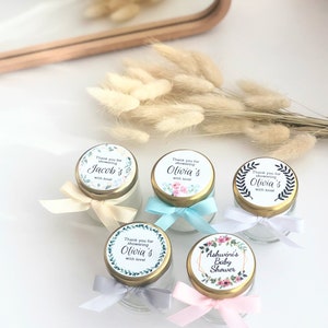 May include: Five small glass jars with gold lids and floral patterned labels. The labels say "Thank you for showering [name]'s with love!" and "Ashwinis Baby Shower".
