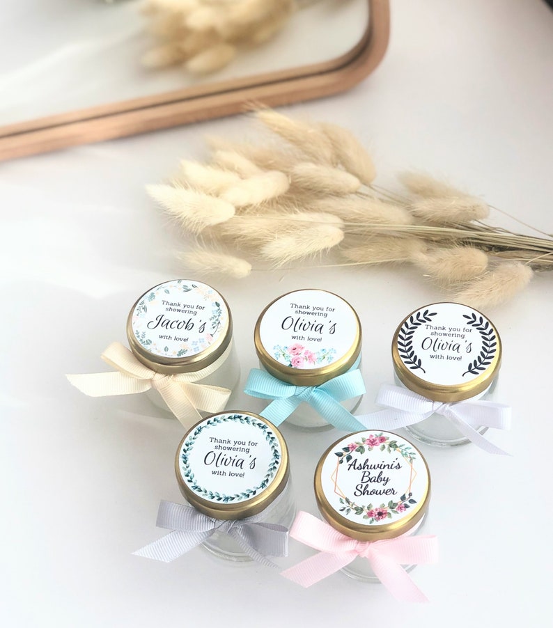 May include: Five small glass jars with gold lids and floral patterned labels. The labels say "Thank you for showering [name]'s with love!" and "Ashwinis Baby Shower".