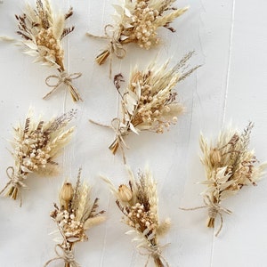 May include: Seven small bouquets of dried flowers in shades of beige and brown, tied with twine. The bouquets are arranged on a white textured background.
