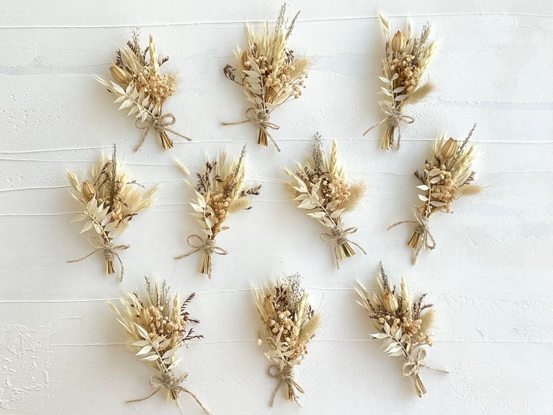 May include: Ten small bouquets of dried flowers in shades of cream and beige, tied with twine. The bouquets are arranged in two rows of five on a white surface.