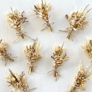 May include: Nine small bouquets of dried flowers in shades of beige and brown, tied with twine. The bouquets are arranged on a white surface.