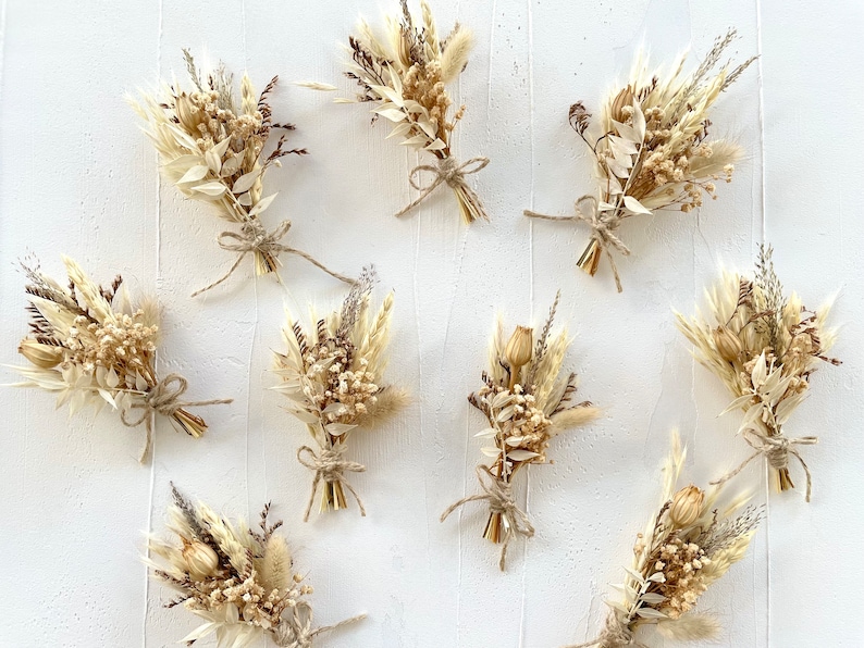 May include: Nine small bouquets of dried flowers in shades of beige and brown, tied with twine. The bouquets are arranged on a white surface.