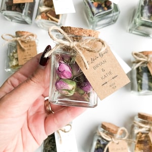 May include: Small glass jars filled with dried flowers and herbs, tied with twine and a brown paper tag that reads "It Love Knew? Bryan & Katie - Rose Tea".