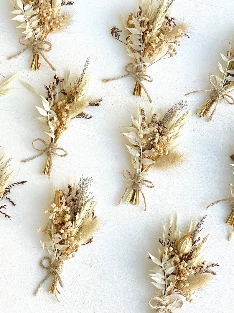 May include: A collection of nine small bouquets of dried flowers, each tied with twine. The bouquets are made up of various shades of beige, cream, and brown dried flowers and grasses.