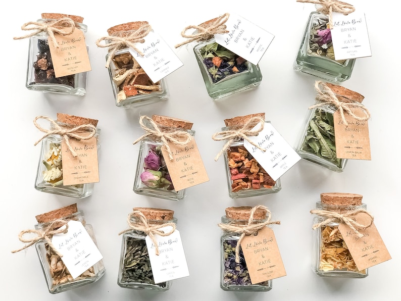 May include: Twelve small glass jars with cork lids, filled with dried herbs and flowers, tied with twine and a small tag that reads "Let's Get Blends Bryan & Katie".