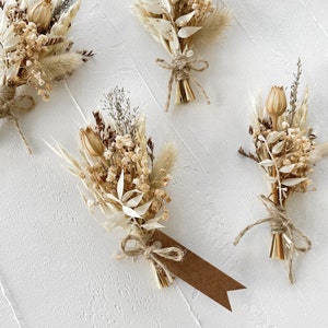 May include: Four small bouquets of dried flowers tied with twine. The bouquets are made of dried grasses, white flowers, and small brown seed pods. Each bouquet has a small brown paper tag attached.
